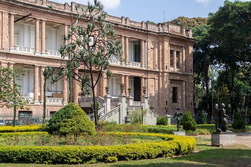 A historic building with columns, a well-manicured garden, and statues. 1