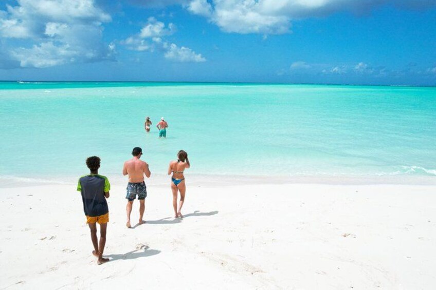 A beach with people walking and swimming in clear turquoise water. 2