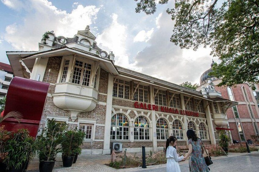 Un edificio histórico con ventanas arqueadas y un balcón, rodeado de plantas en macetas y una estructura roja. 4