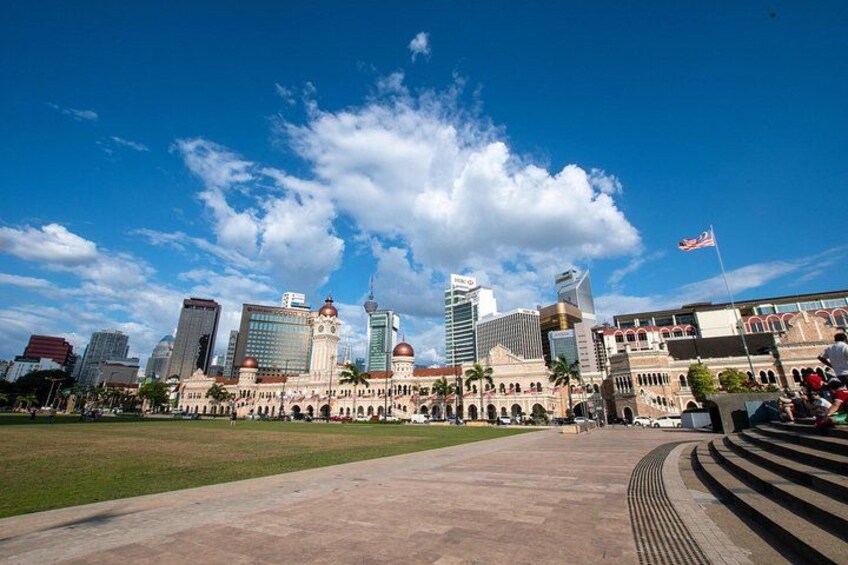 Un horizonte urbano con edificios modernos e históricos, una amplia plaza abierta y un cielo azul despejado. 5