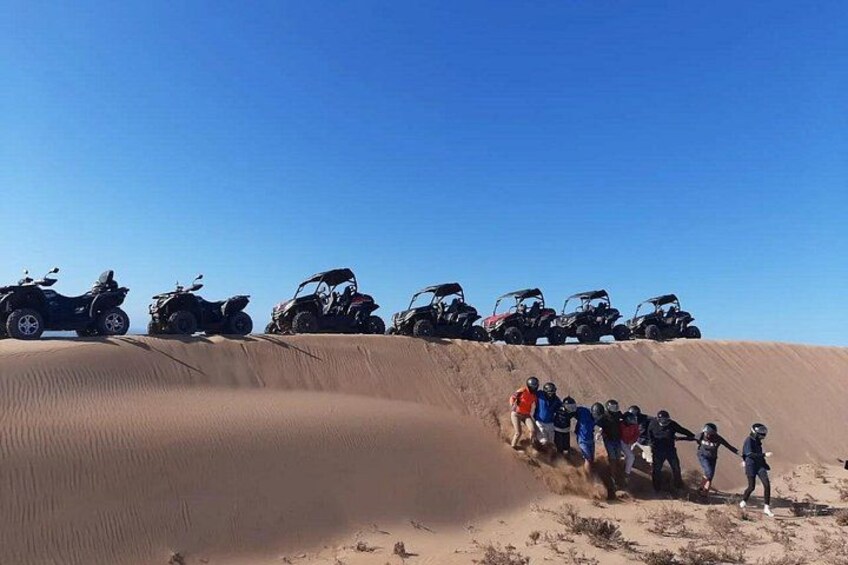 A group of people on a sandy slope with ATVs parked at the top. 3