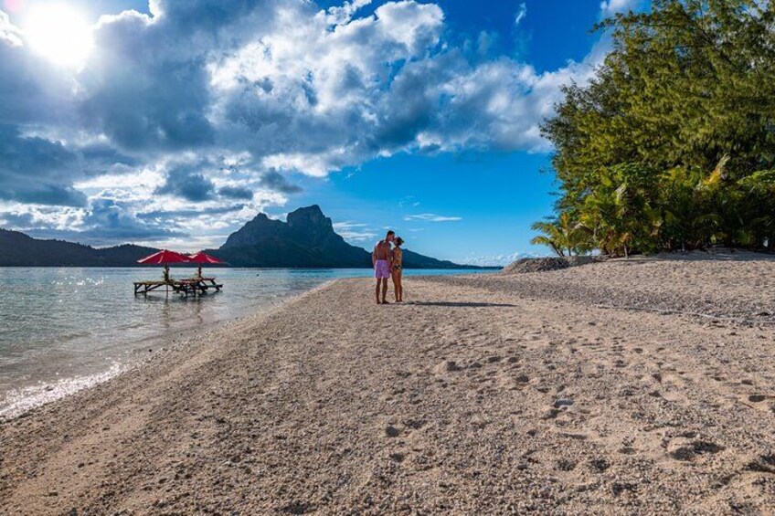 Une plage avec un parasol rouge, une personne debout et une montagne en arrière-plan. 2