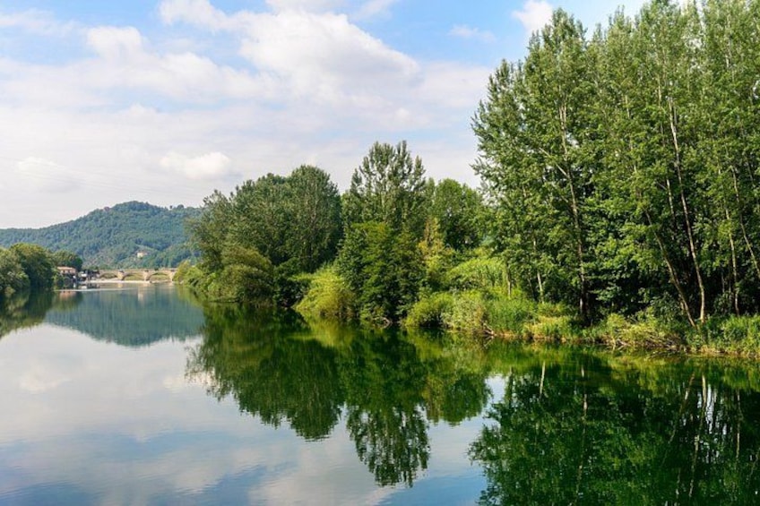 A calm river reflecting trees and a bridge in the distance. 3