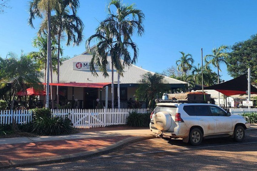 Ein Restaurant mit weißem Zaun, Palmen und einem geparkten SUV. 3