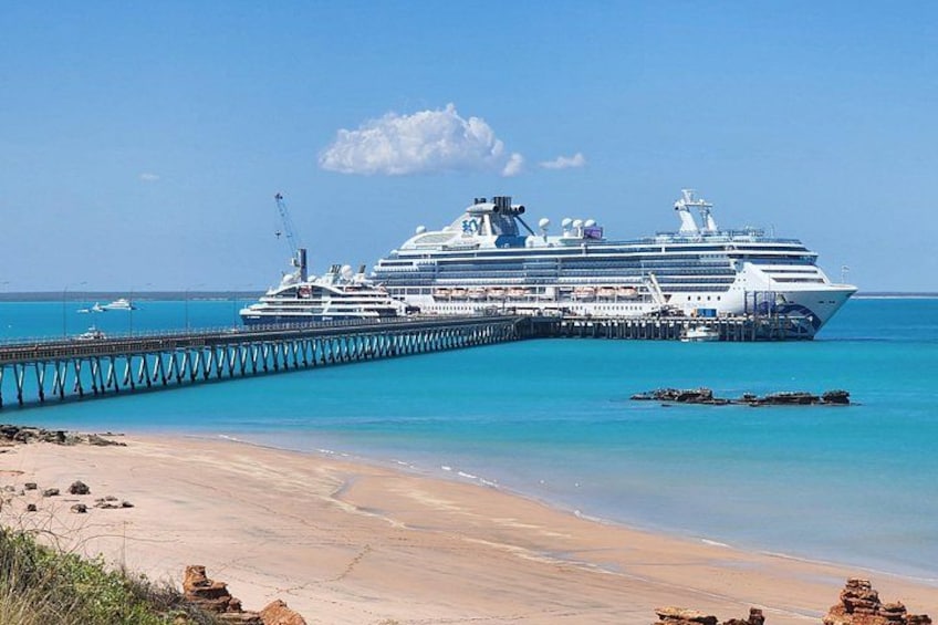 Ein großes Kreuzfahrtschiff liegt an einem Steg, im Vordergrund türkisfarben klares Wasser und ein Sandstrand. 4