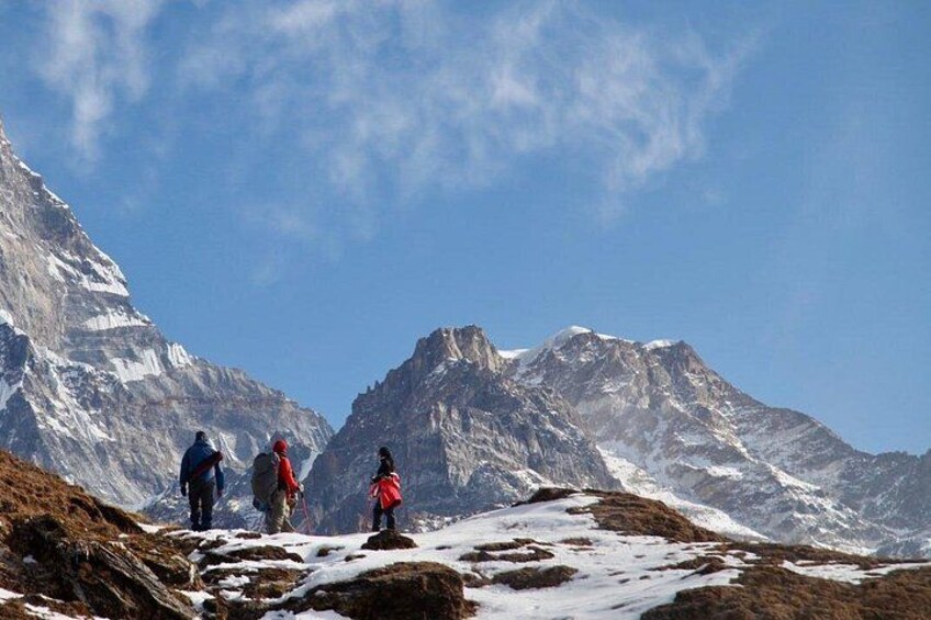 A group of hikers on a snow-covered mountain trail with rocky terrain and snow-capped peaks in the background. 5