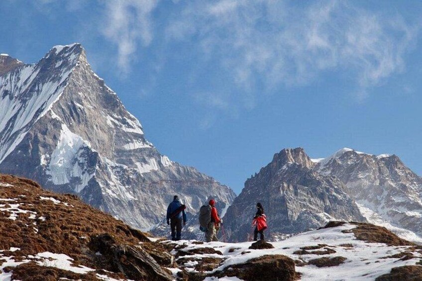 Three hikers on a snow-covered mountain trail with a prominent peak in the background. 4