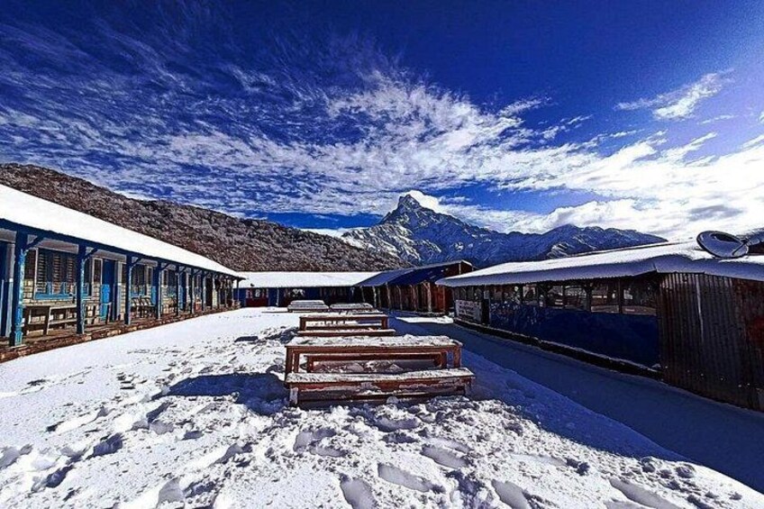 A snow-covered train station with wooden benches, a clear sky, and mountains in the background. 3