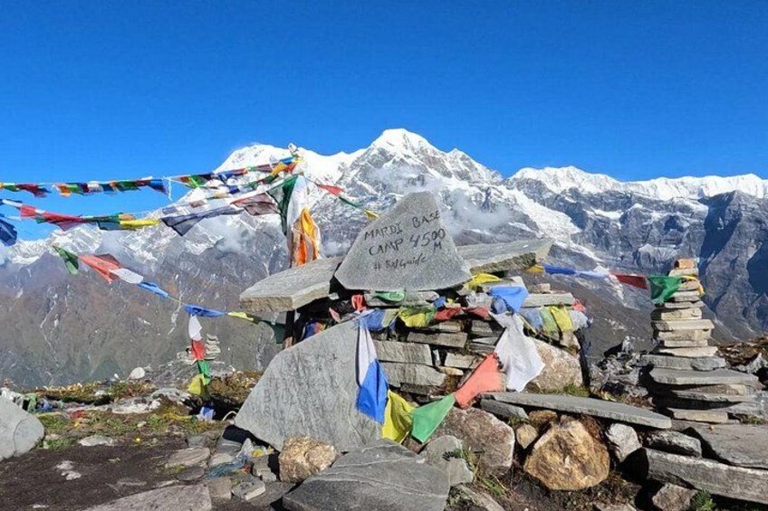 A mountain base camp with a sign, prayer flags, and a stone cairn. 2