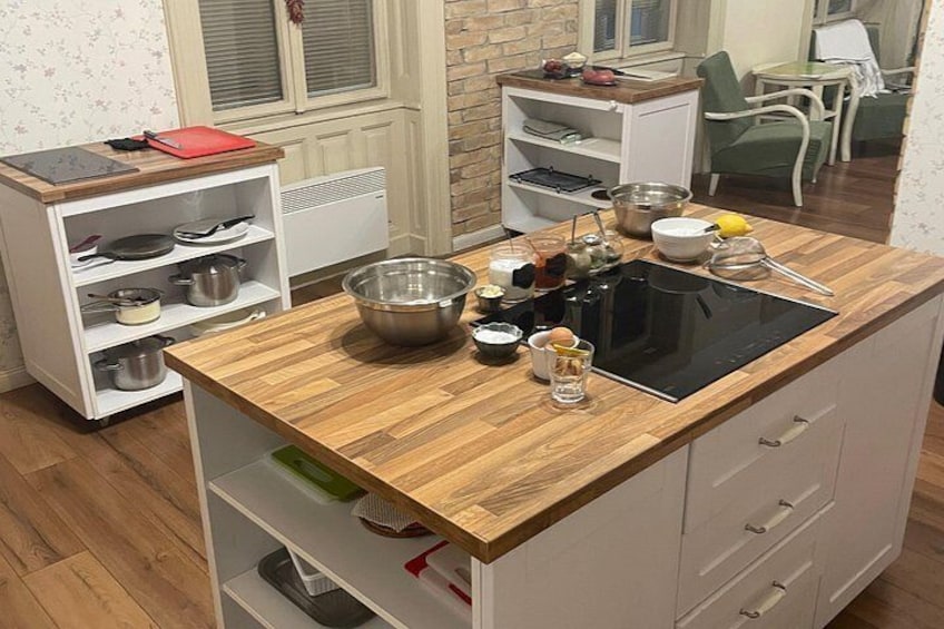 A kitchen with a wooden countertop, a black induction cooktop, and various kitchen utensils and appliances. 4