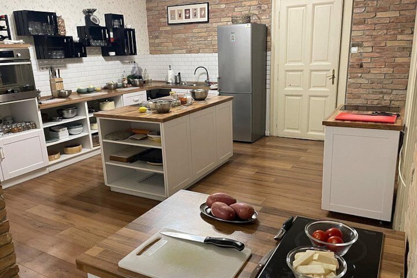A kitchen with wooden flooring, white cabinets, a central island with a cutting board, and various kitchen items. 3
