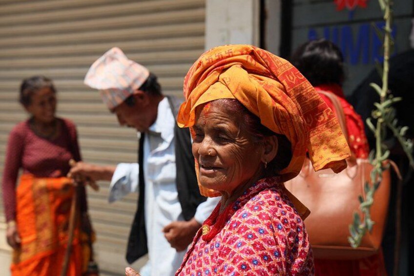 Una persona con camisa estampada y turbante, con un edificio y otras personas al fondo. 4