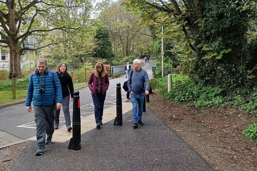 A group of people walking on a path with bollards, surrounded by trees and greenery. 2