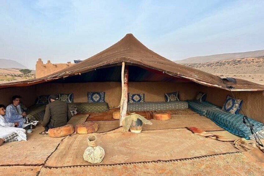 A traditional tent with a conical roof, patterned cushions, and a woven rug on the ground. 1