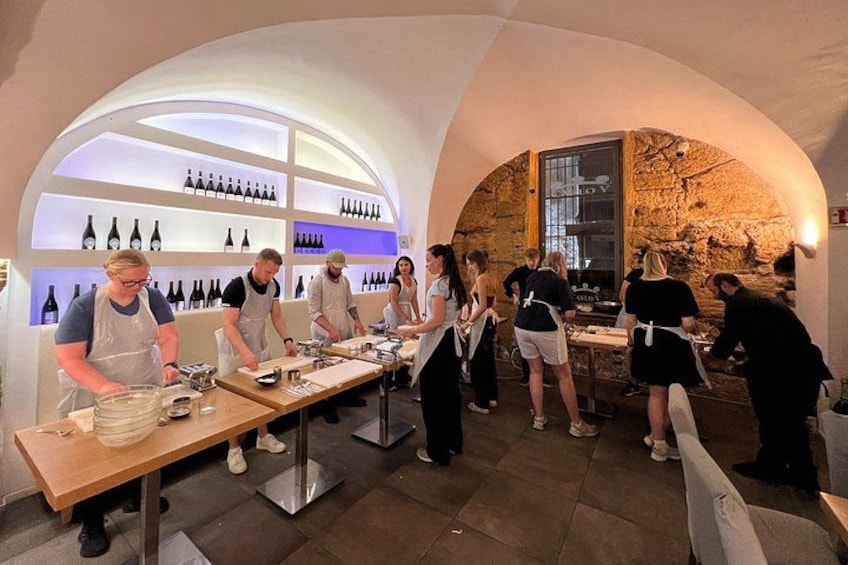 Un grupo de personas en una cocina con botellas de vino en estantes y una pared de piedra. 2