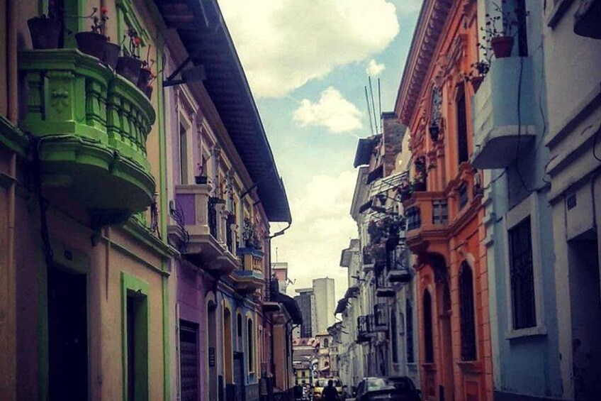 Una calle estrecha flanqueada por edificios coloridos, algunos con balcones y plantas colgantes. 5