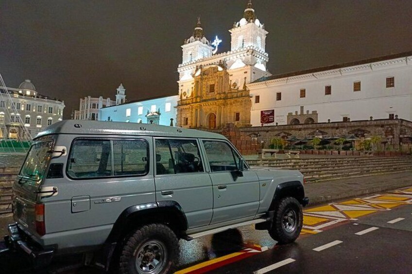 Un SUV plateado estacionado sobre una carretera mojada, con un edificio histórico al fondo. 1