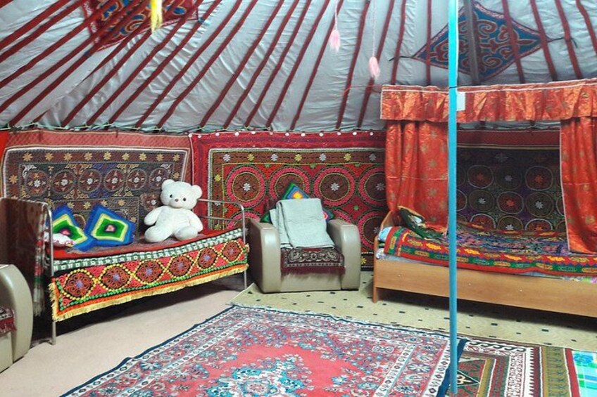 A yurt interior with a bed, a chair, a rug, and a stuffed bear. 2