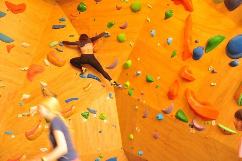 Una persona arrampica su un muro di legno con appigli colorati. 5