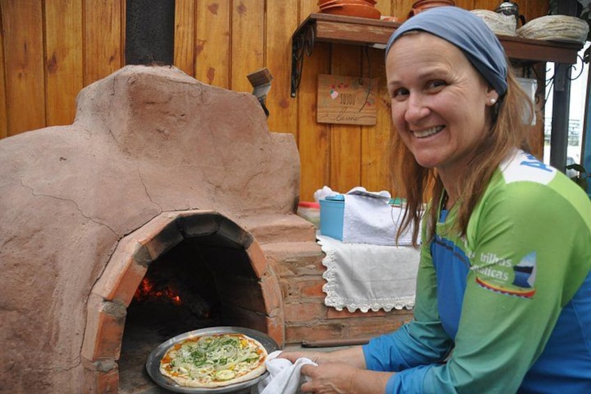 Una donna con una camicia verde e blu sta preparando una pizza in un forno a legna. 3