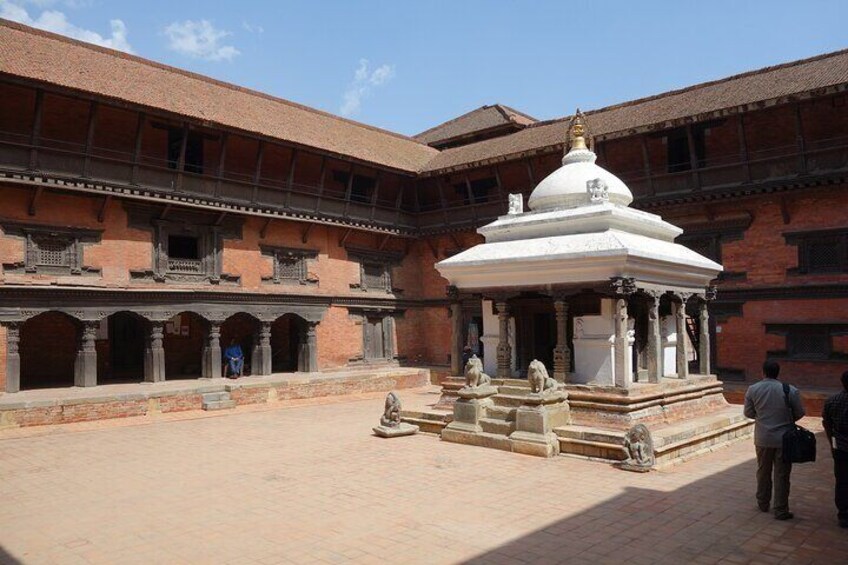 A courtyard with a white stupa, stone statues, and a brick building with multiple balconies. 4