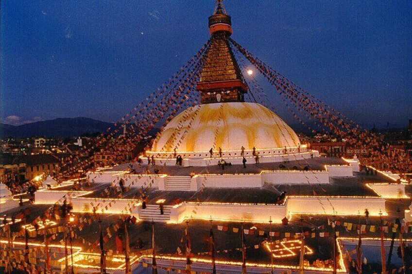 A large illuminated stupa with a golden dome and a spire, surrounded by a crowd of people. 1