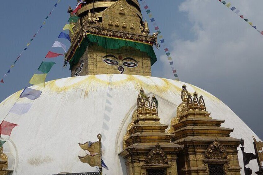 A large white stupa with golden decorations and a green roof, surrounded by colorful prayer flags. 3