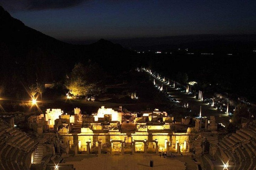 An ancient amphitheater with stone seating and a stage, illuminated by artificial lights. 5