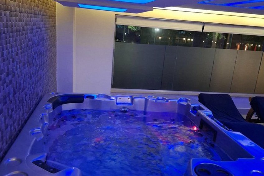 A hot tub with blue lighting, a brick wall, and a window overlooking a balcony. 2