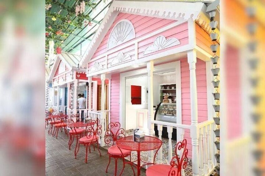A pink and white building with red chairs and tables, a glass display case, and a white door. 3