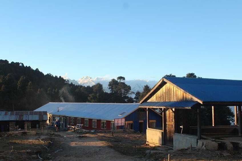 A rural area with wooden buildings, a dirt road, and a mountain range in the background. 4