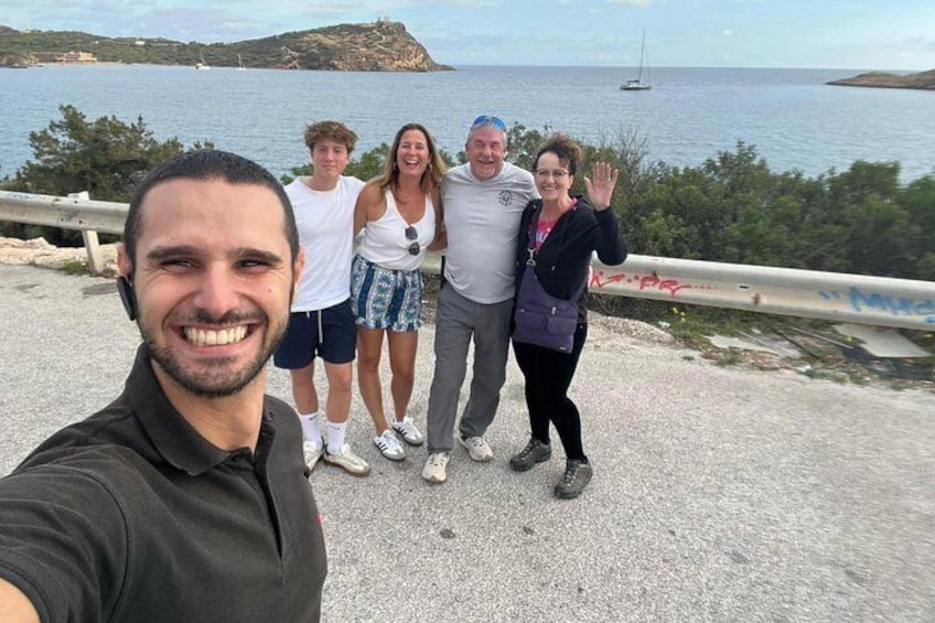 Un groupe de personnes se tient au bord d’une route côtière, d’où l’on aperçoit la mer et une petite île au loin. 2