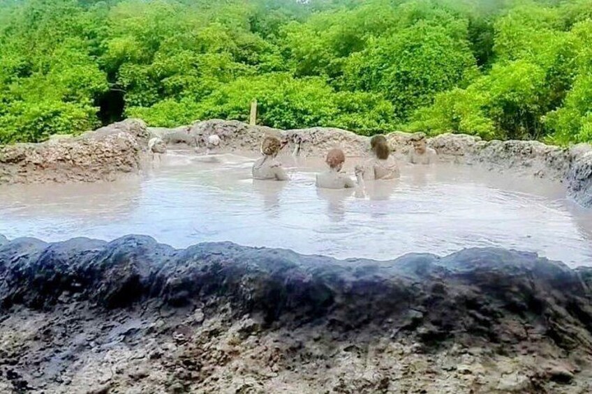 Una fuente termal natural con personas bañándose, rodeada de abundante vegetación. 3