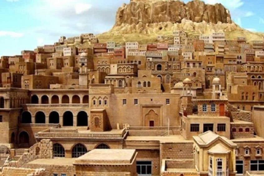 A densely packed cityscape with historic architecture, a prominent rocky hill in the background, and a clear sky. 5