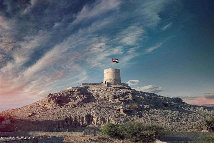 A historic tower with a flag on top, surrounded by rocky terrain and sparse vegetation. 5