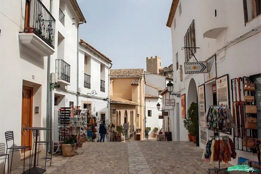A narrow street with shops and a museum sign. 3