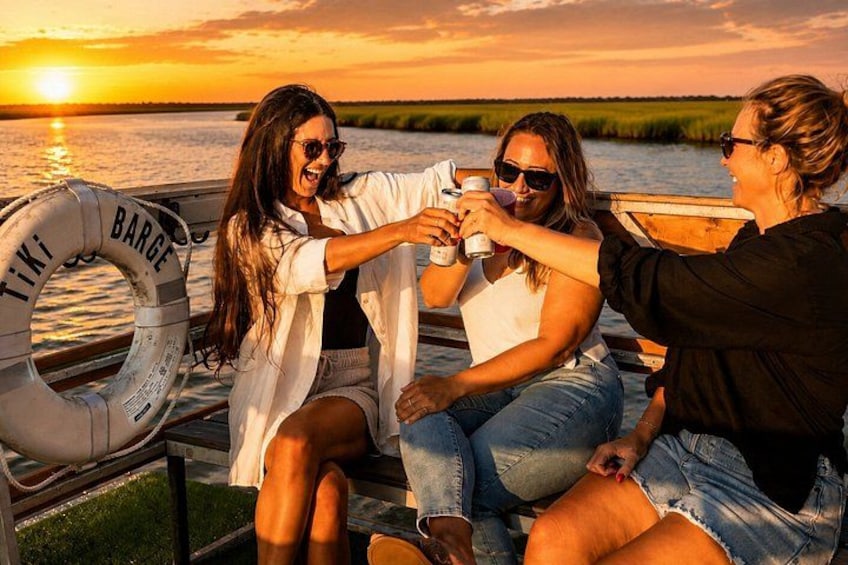 Drie personen proosten met drankjes op een boot bij zonsondergang. 5