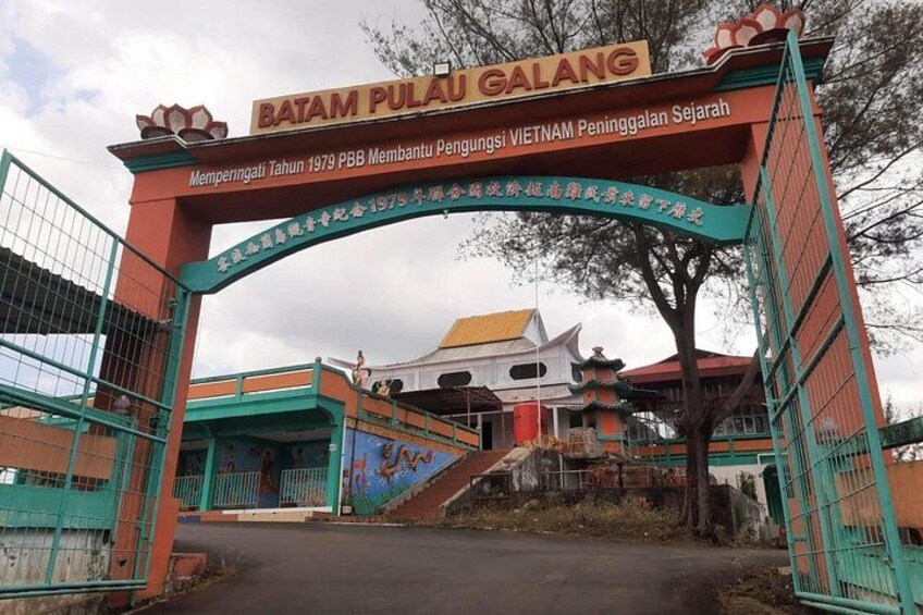 Una puerta con un letrero que dice 'BATAM PULAU GALANG' y un edificio tradicional al fondo. 5