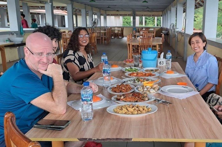 Un grupo de personas cenando en una mesa al aire libre cubierta, con varios platos y botellas de agua. 2