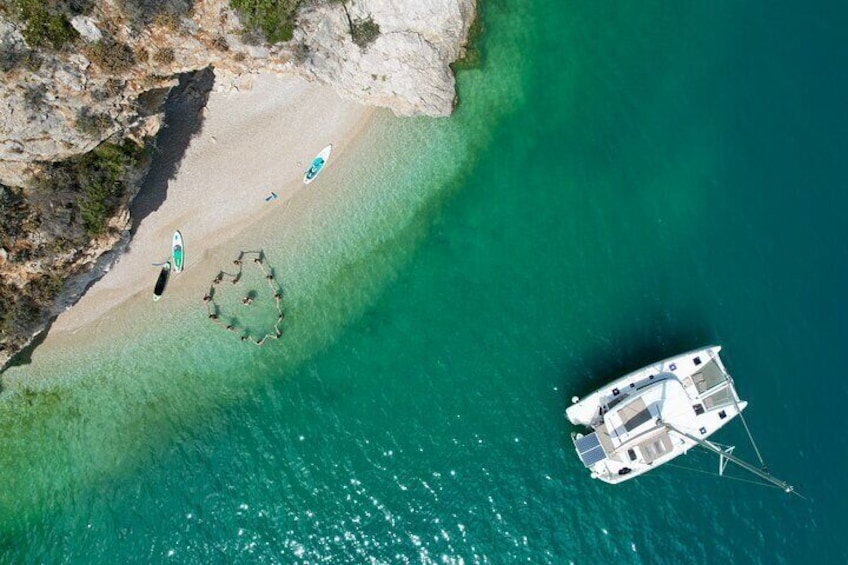 Oversigtsbillede af en strand med en båd forankret nær kysten, omgivet af klart turkis vand og klippefremspring. 1