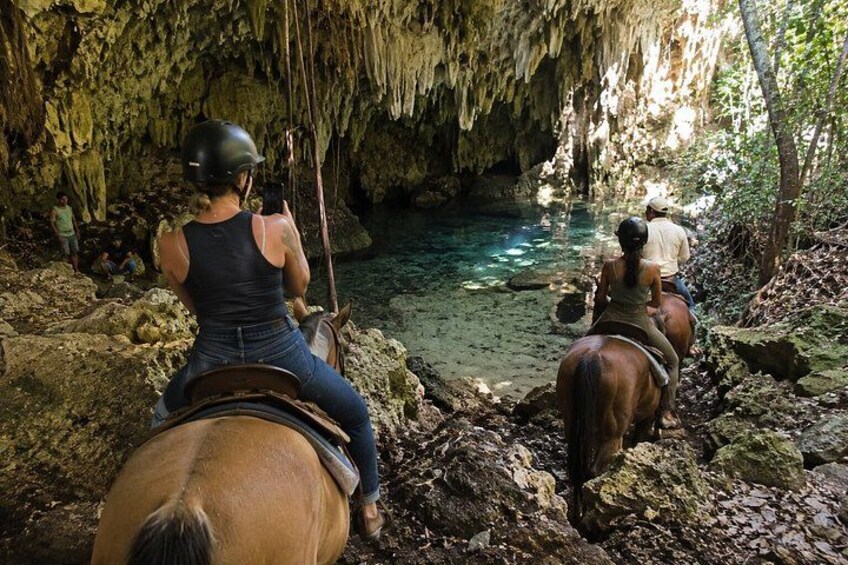 People riding horses through a cave with a clear water stream. 2