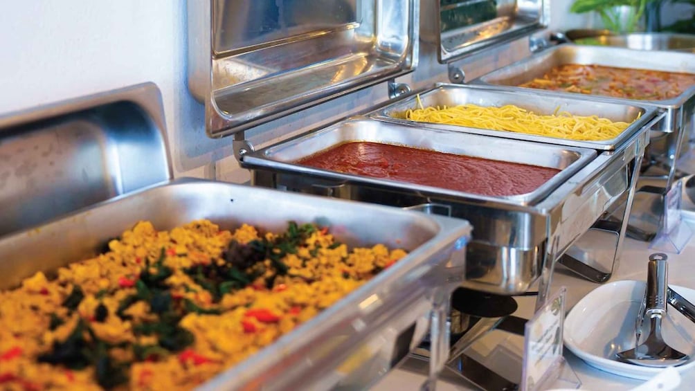 Ein Buffet mit verschiedenen Speisen, darunter Pasta, rote Soße und ein Gericht mit Gemüse und Fleisch. 3