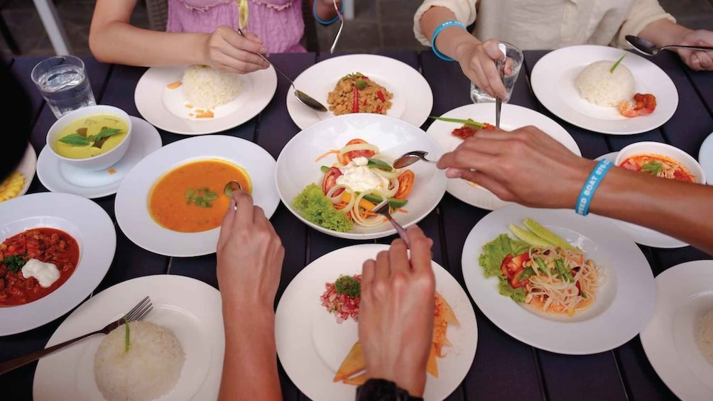 Eine Gruppe von Menschen isst an einem Tisch mit verschiedenen Gerichten, darunter Reis, Suppe und Salate. 2