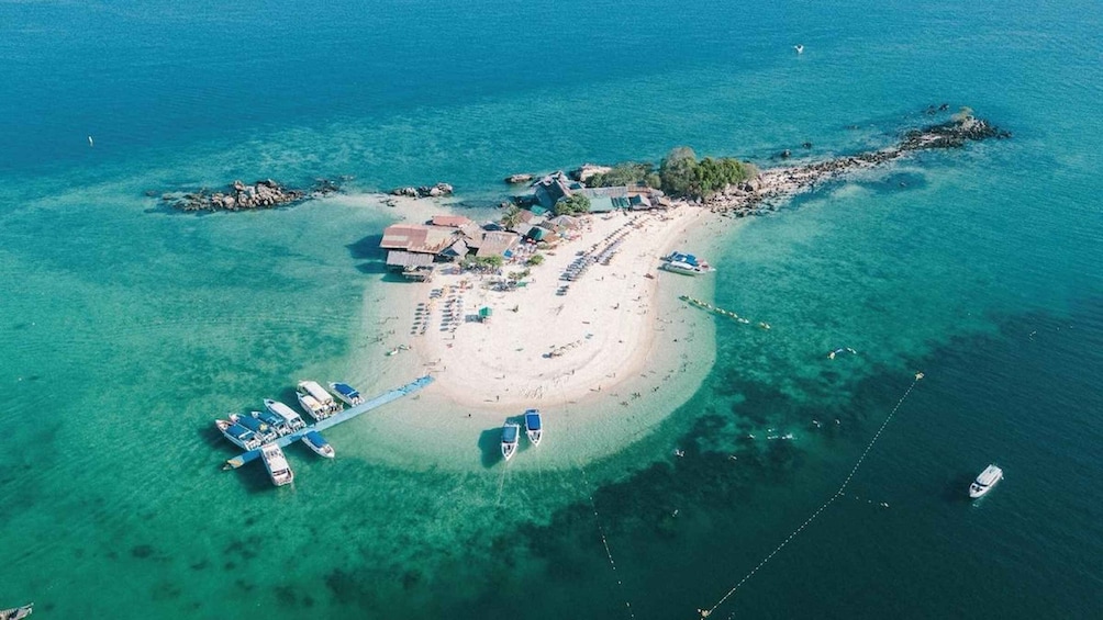 Eine Luftaufnahme einer tropischen Insel mit klarem türkisblauem Wasser, einem Sandstrand, einer kleinen Siedlung mit Gebäuden und mehreren Booten, die in der Nähe der Küste vor Anker liegen. 4