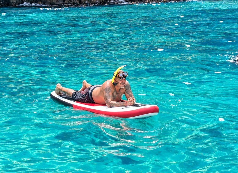 Une personne allongée sur un radeau gonflable rouge et blanc, dans une eau d’un bleu limpide. 2