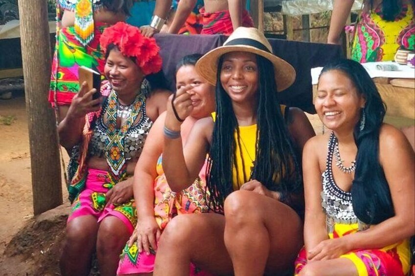 A group of people sitting on a bench outdoors, wearing colorful traditional attire. 4