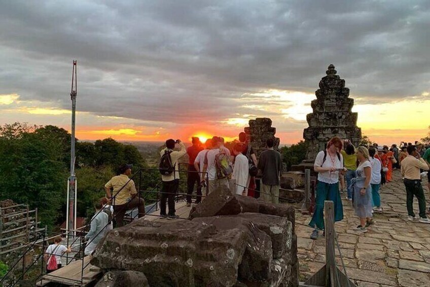 A sunset at a historical site with visitors, a stone structure, and a watchtower. 3