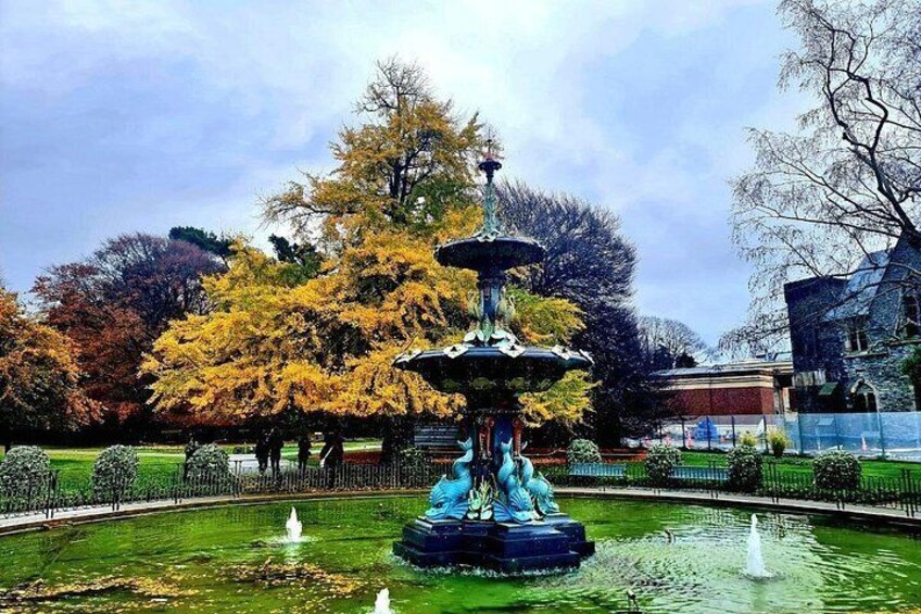 A fountain with a statue, surrounded by a pond and trees with autumn foliage. 4