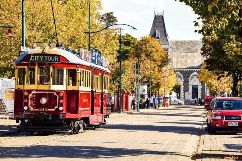 Un tranvía rojo y amarillo con la leyenda 'CITY TOUR' circulando sobre rieles, con árboles otoñales y un edificio histórico al fondo. 3