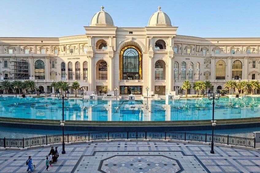 Un edificio grande con una entrada arqueada central, un área de piscina al frente y palmeras alrededor. 5
